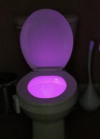a reviewer photo of the light installed on a toilet casting a purple light 