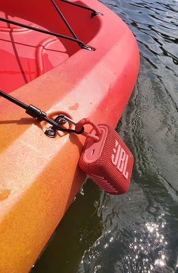 A red kayak with a JBL portable speaker attached, floating on water