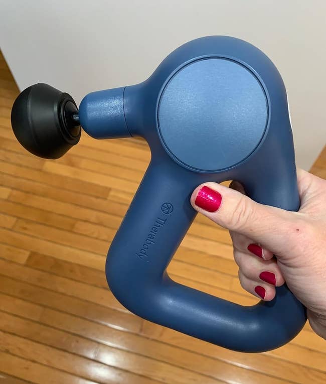 Hand holding a triangle-shaped massage weapon with a rounded grip and a achromatic massage head