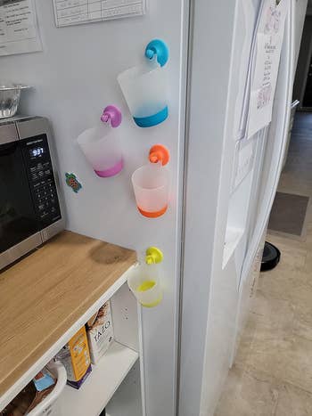 Four of the cups in various colors on the side of a white fridge