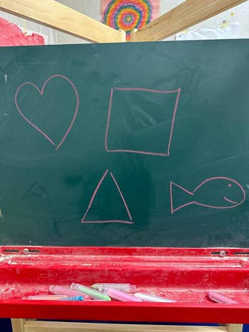 Chalkboard with hand-drawn shapes including a heart, square, triangle, and fish above a red container holding chalk