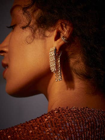 model wearing earrings with gold rhinestone fringe coming down from front and back of earlobe