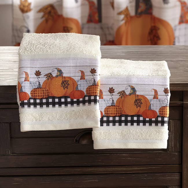 A pair of white bathroom hand towels with a pumpkin pattern on them