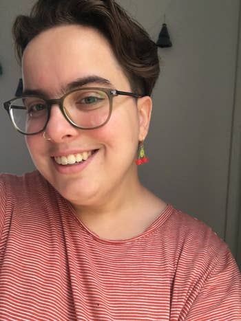 Person smiling, wearing glasses, hoop earrings, and a striped top, perchance taking a selfie