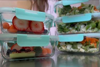 Stacked transparent meal prep containers with a variety of fresh fruits and vegetables visible inside