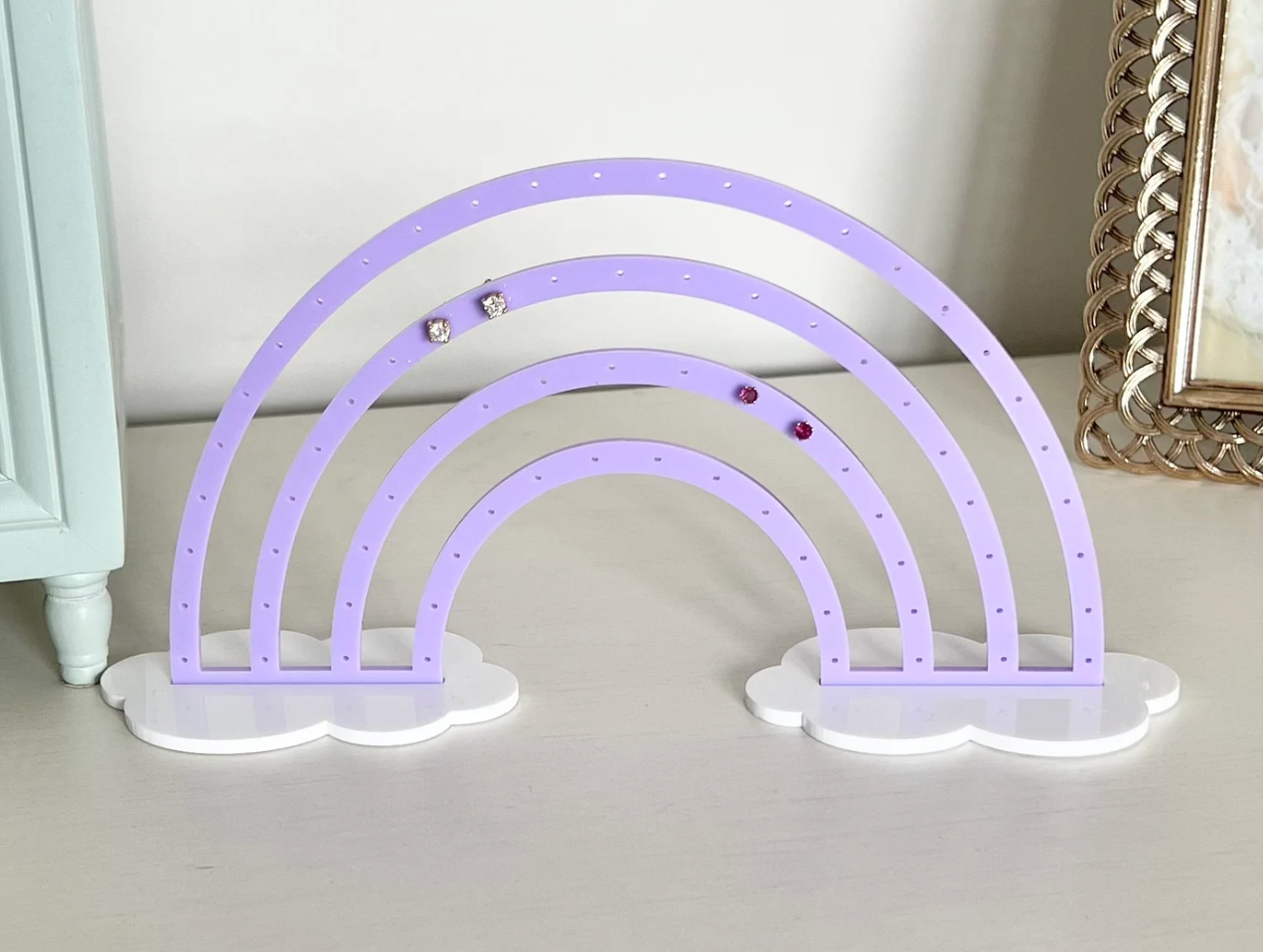 Purple rainbow-shaped earring holder with clouds on top of a white table