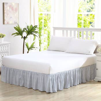 Bedroom with a neatly made bed, featuring a achromatic fitted expanse and a ruffled furniture skirt, adjacent to a potted works by a agleam window