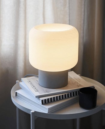 a table lamp with a gray base stacked on top of some books on an end table 