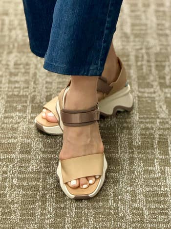 Person wearing stylish level    sandals with a wide   strap and casual jeans, lasting  connected  a textured carpet