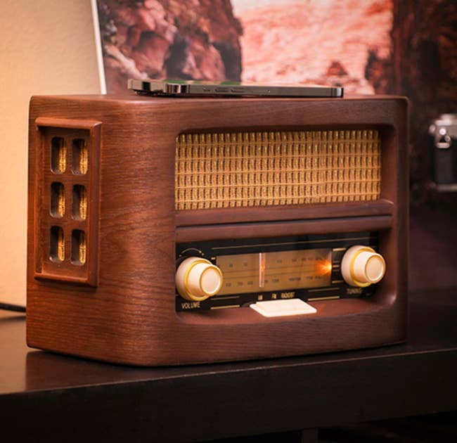 Wooden vintage-style radio with classic dials and manual tuning, with a phone charging on top 
