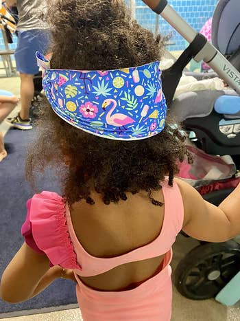 Child from behind wearing a floral visor and pink swimsuit with ruffles