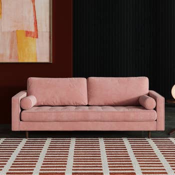Pink sofa with two cushions in a room with an abstract painting and striped rug. Ideal for chic home decor