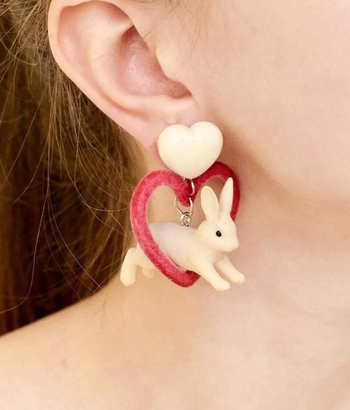 model wearing earrings with large white heart post and dangling leaping white bunny jumping through pink velvet heart