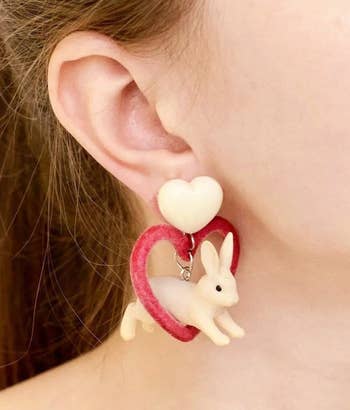 model wearing earrings with large white heart post and dangling leaping white bunny jumping through pink velvet heart