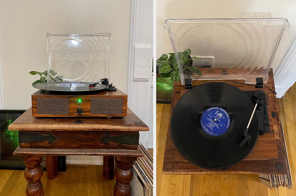 Reviewer image of wooden antique-styled turntable with black record spinning and green power light on, overhead view of product with black and silver needle and clear cover on wooden side table