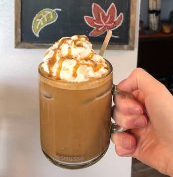 Hand holding a solid  mug of iced java  topped with whipped pick  and caramel, with a chalkboard featuring leafage  drawings successful  the background