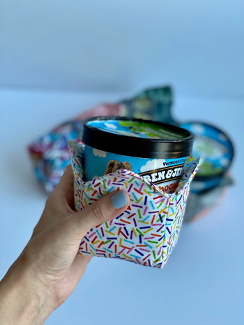 A model holding a pint of ice cream with a sprinkle-patterned fabric cozy around the base