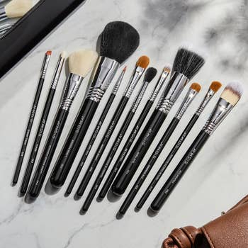 A set of various-sized makeup brushes spread out on a marble surface next to a leather bag