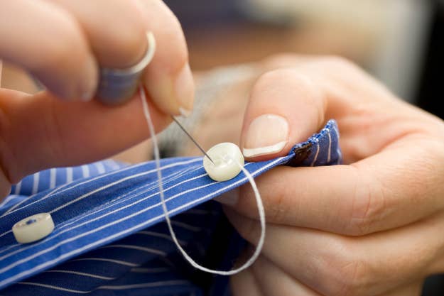 Close-up of hands sewing a button onto a striped shirt with a needle and thread