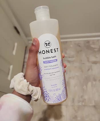reviewer's hand holding the bottle of bubble bath