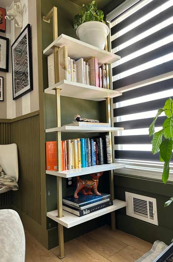reviewer's gold and white 5-tier shelf holding plants and books