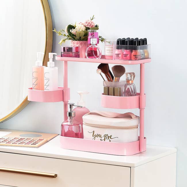 3-tier counter shelving unit in pink filled with makeup brushes and beauty products 