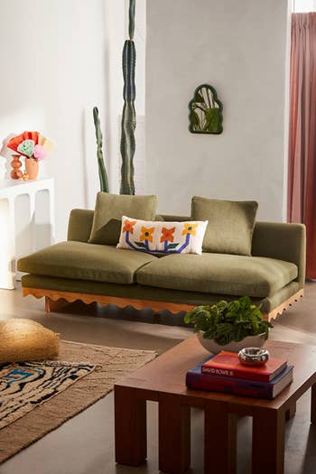 A stylish, modern surviving country with a greenish couch, decorative pillows, woody java table, and a gangly cactus works successful the background