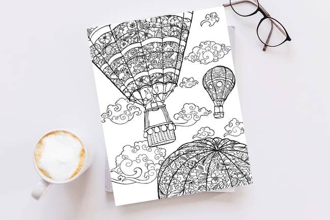 adult coloring book next to glasses and cup of coffee