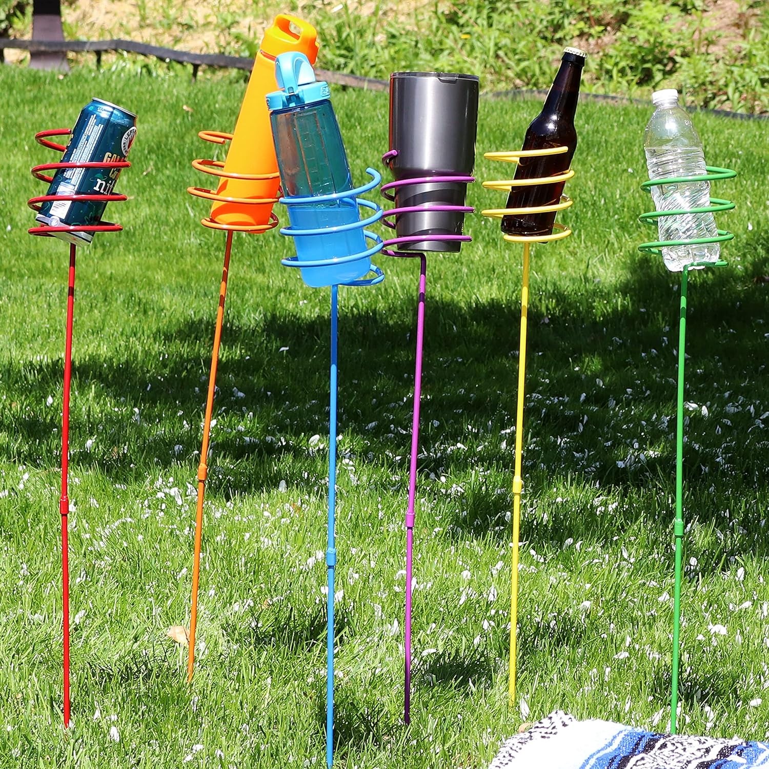 Five garden stakes with spiral holders containing different types of drinkware in a grassy yard