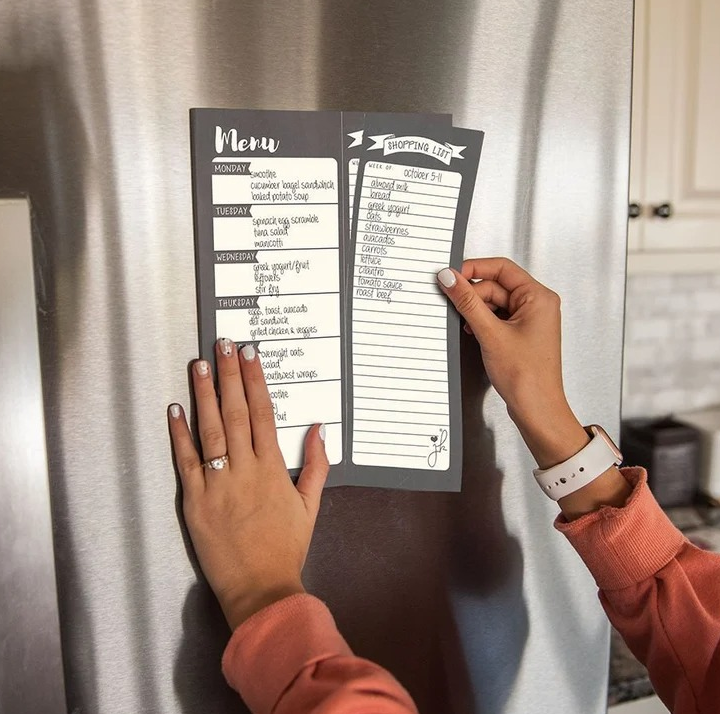 a model tearing the shopping list portion of the dual column notepad off as it hands on the fridge 