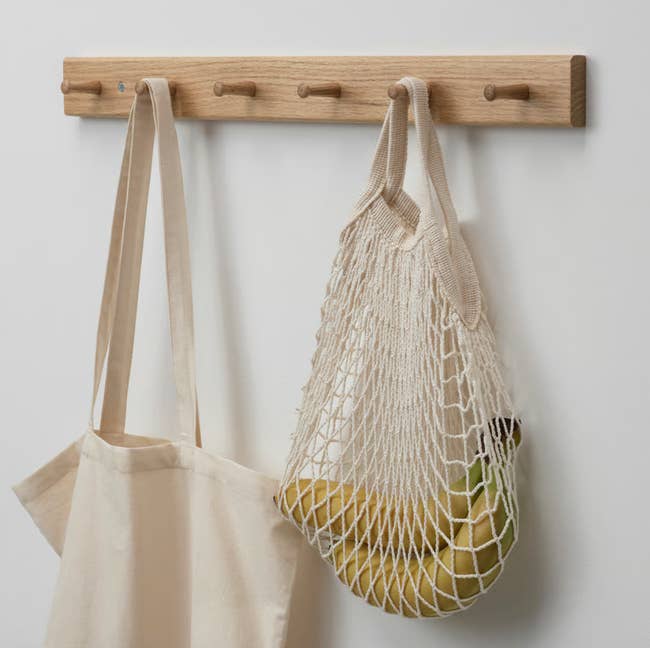 Canvas tote and mesh container  with bananas hanging connected  a woody  partition  rack with pegs