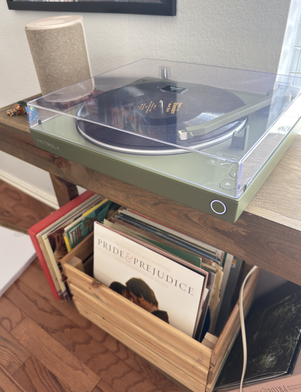 Turntable playing a grounds   adjacent  to a woody  crate of vinyl albums, including 