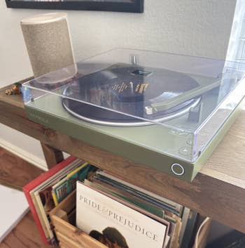Turntable playing a grounds adjacent to a woody crate of vinyl albums, including