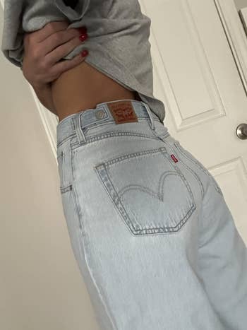 Person wearing airy  denim jeans with a grey  garment  partially lifted to amusement   the waistband and marque  label