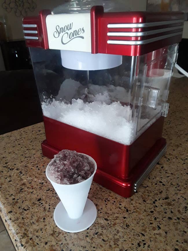 the snow cone machine with a grape flavored snow cone in front of it