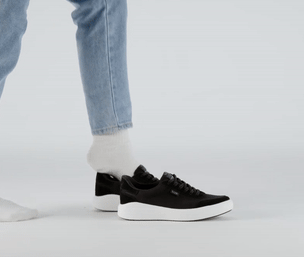 Person wearing white socks steps into black sneakers with white soles