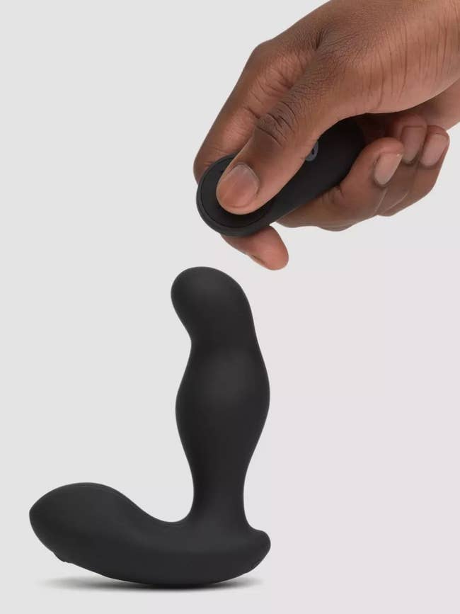 Hand holding black wireless remote next to black prostate vibrator