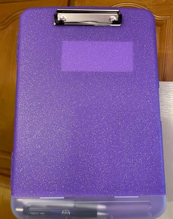 A glittery purple clipboard with a metal clip on a wooden surface