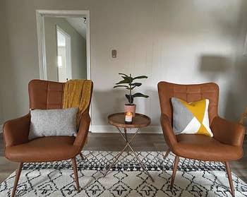 reviewer photo of the pair of faux leather chairs holding pillows and throw blankets