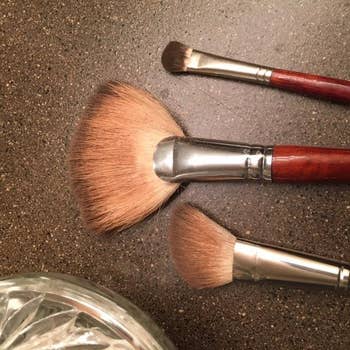 Three constitution  brushes with woody  handles are laid retired  adjacent  to a solid  jar connected  a textured surface