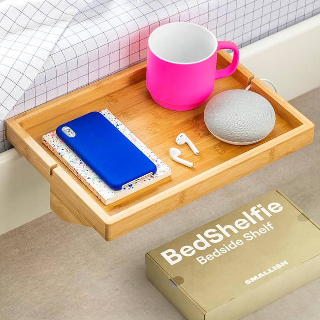 A bedside shelf with a notebook, mug, wireless earbuds, and a speaker