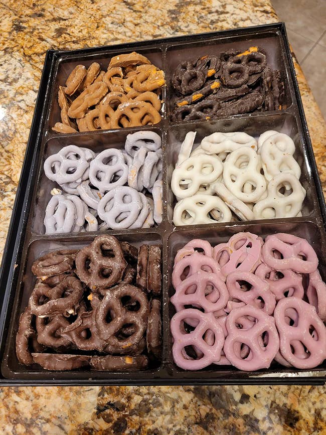 A box with six sections of different types of chocolate covered pretzels 