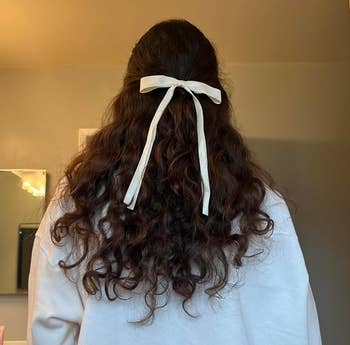 Person facing mirror with curly hair tied by a white ribbon