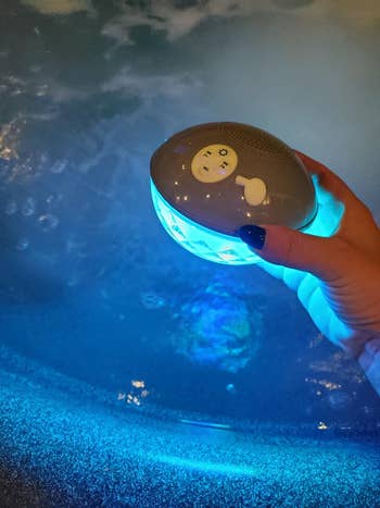 Hand holding a floating waterproof Bluetooth talker supra a lit pool, highlighting versatility for h2o use