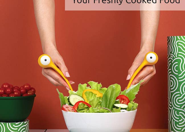 Person using salad servers with bird-shaped heads to mix a bowl of fresh salad