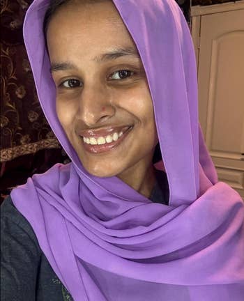 Person smiling, wearing a purple headscarf, indoors
