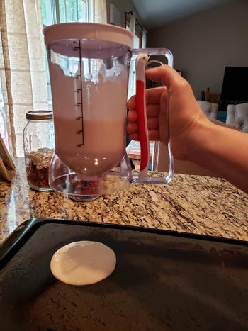 reviewer using the batter dispenser to pour a perfect circle of pancake batter onto a griddle