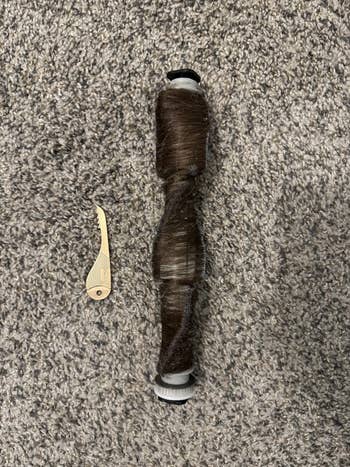A beige grip seam ripper beside a spool of brownish thread connected a textured surface
