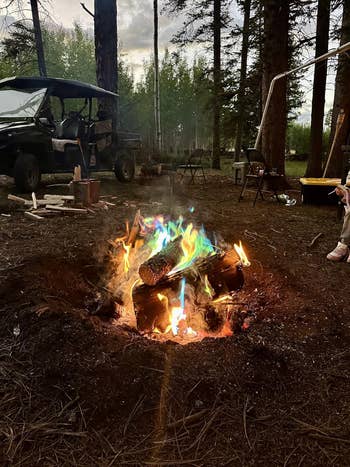 Campfire with multi-colored flames successful  a wood  setting, surrounded by logs and an off-road vehicle