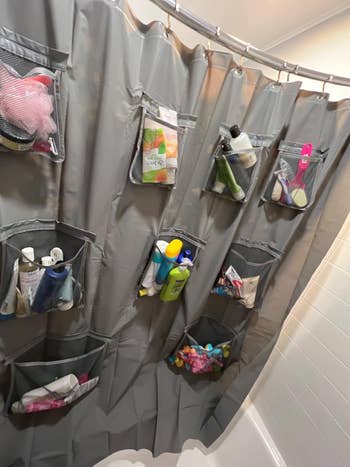 gray shower curtain with multiple pockets filled with various bath items